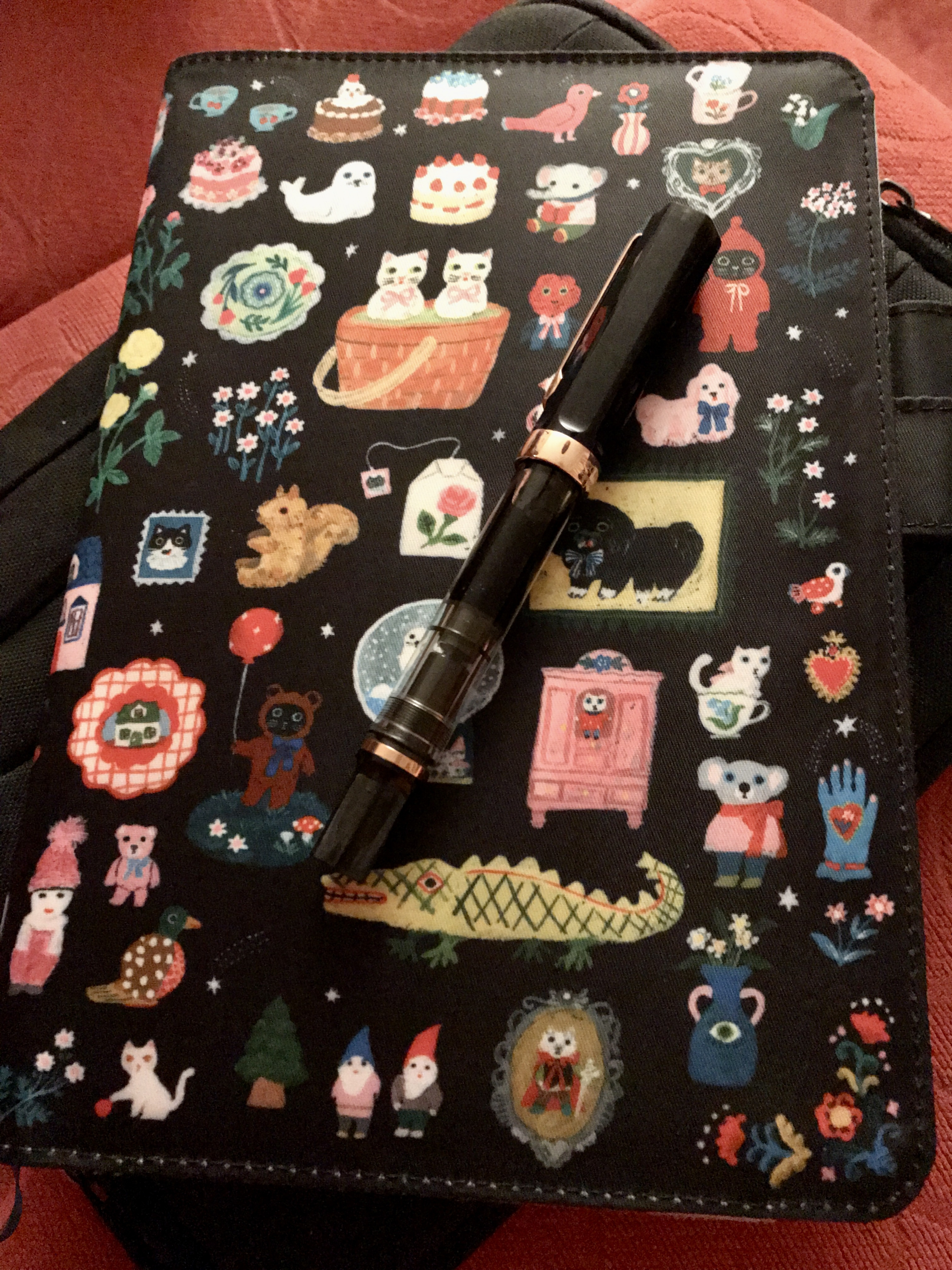 A black fountain pen resting on top of a paper planner inside a brightly coloured soft cover decorated with lots of cute designs.