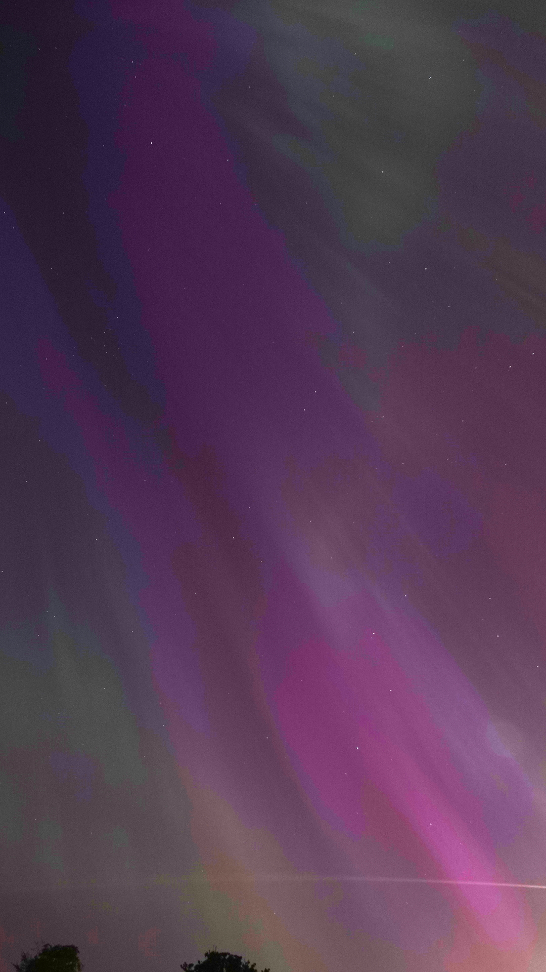 A portrait shaped view of the night sky with purple and pink aurora streaks sweeping diagonally down from top left to bottom right, and greens and blues around