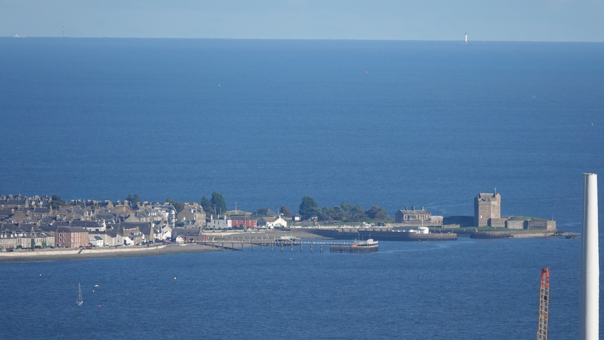 Hazy sunny view looking across blue River Tay towards Broughty Castle, and beyond that the North Sea and in the distance white Bell Rock Lighthouse